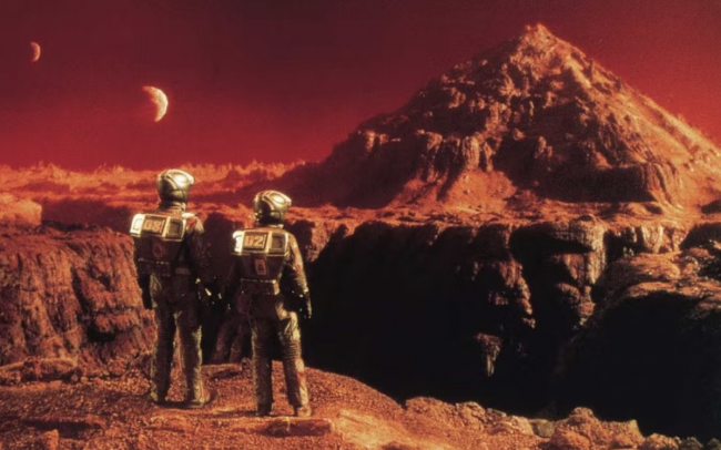 a still from the movie total recall of two characters in spacesuits looking out over Mars